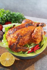 Juicy baked chicken served over fresh herbs with lemon and vegetables. A close-up of a whole grilled chicken.