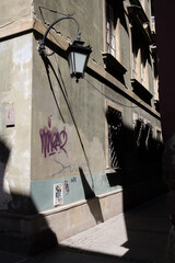 Wall-mounted streetlight casting shadow over a graffiti-covered wall in Warsaw, a gritty urban moment.