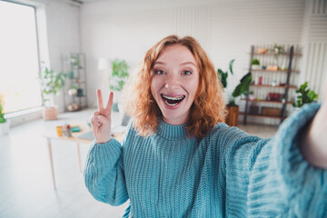 Young woman with red hair smiling in a daylight living room wearing a knitted sweater