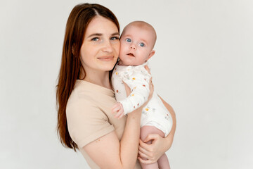 mom with a baby on a white isolated background and on the bed, a place for text, a young mother gently hugs her little baby girl, maternal love and care