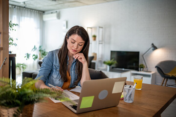 Obraz premium Focused freelancer working from home on laptop and taking notes