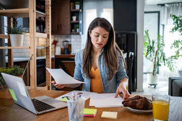Focused businesswoman reviewing documents while working remotely from home