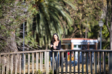 brunette woman, young and beautiful dressed in casual clothes leaning on the railing of a wooden...