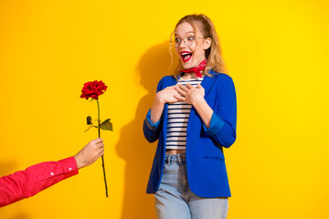 Joyful young woman surprised by a red rose gift against a vibrant yellow background