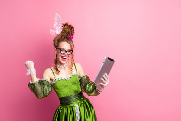 Young woman in antique-inspired green dress holding digital tablet against pink background, blending past elegance with modern technology