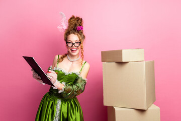 A cheerful woman in a baroque-style green dress with a clipboard posing against a pink background © deagreez
