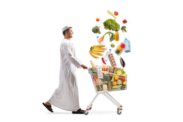 Middle eastern man pushing a shopping cart with falling food assortment