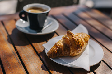 Cup of black coffee and a tasty croissant on a table in a street cafe. Selective focus.