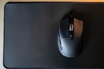 A wireless gaming mouse positioned on a black mouse pad in a well-lit workspace during the afternoon