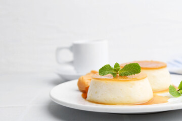 Tasty puddings with caramel sauce served on white tiled table, closeup. Space for text