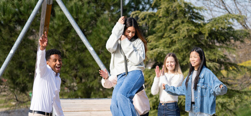 Young latin woman swinging on zip line while excited diverse friends cheer her on