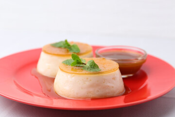 Tasty puddings with caramel sauce served on white tiled table, closeup