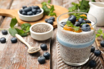 Delicious chia pudding with blueberries, peaches and mint in glass on wooden table, closeup