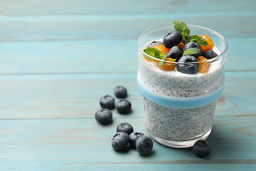 Delicious chia pudding with blueberries, peaches and mint in glass on light blue wooden table, closeup. Space for text