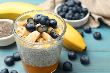 Delicious chia pudding with blueberries, banana and oatmeal in glass on light blue wooden table, closeup