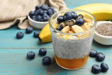 Delicious chia pudding with blueberries, banana and oatmeal in glass on light blue wooden table, closeup