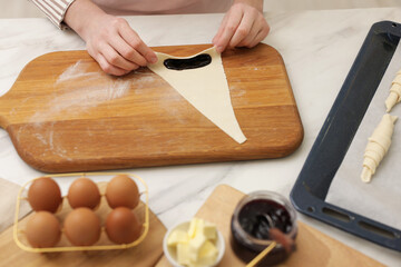 Woman rolling croissant with jam from fresh dough at white marble table, closeup
