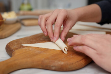 Woman rolling croissant from fresh dough at light table indoors, closeup