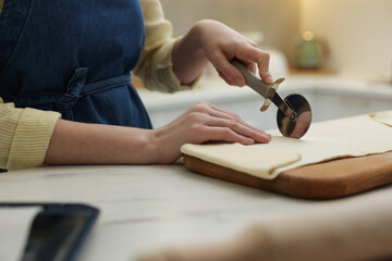 Woman cutting dough at light marble table indoors, closeup. Making croissants
