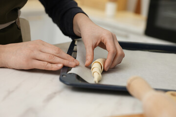 Woman putting raw croissant onto baking sheet at white marble table indoors, closeup
