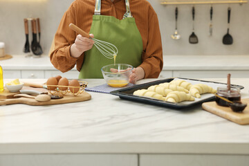 Woman whisking egg wash near raw croissants at white marble table in kitchen, closeup