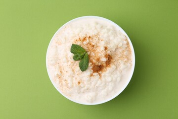 Tasty rice pudding with cinnamon and mint in bowl on green background, top view