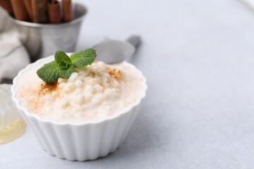 Tasty rice pudding with cinnamon and mint on light grey table, closeup. Space for text