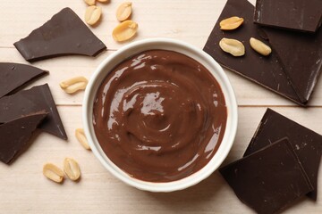 Tasty pudding, pieces of chocolate and peanuts on white wooden table, flat lay