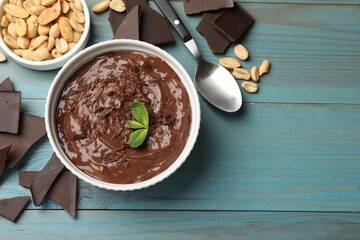 Tasty chocolate pudding in bowl and ingredients on light blue wooden table, flat lay. Space for text