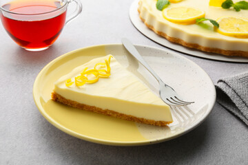 Piece of tasty lemon cheesecake and fork on grey textured table, closeup