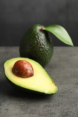 Whole and cut avocados on grey textured table, closeup