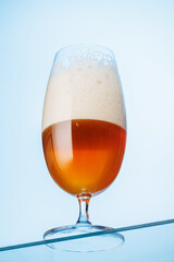 A tall glass of beer with a golden hue and frothy head, on a blue background
