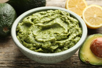 Tasty avocado dip in bowl and fruits on wooden table, closeup