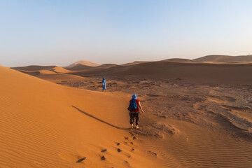 Two people trekking travel through the Sahara Desert amidst sand dunes and arid landscape