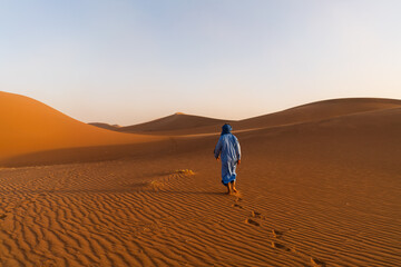 Nomadic Berber man walking on the immense sand dunes of the Sahara Desert dressed in a traditional indigo blue tunic