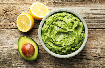 Tasty avocado dip in bowl and fruits on wooden table, flat lay