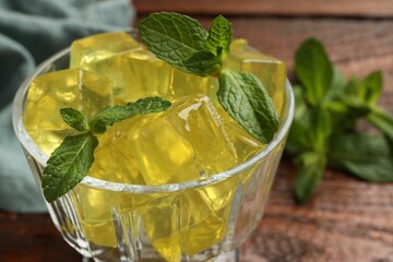 Yellow jelly cubes in dessert bowl and mint on table, closeup