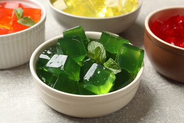 Different jelly cubes in bowls on grey table, closeup