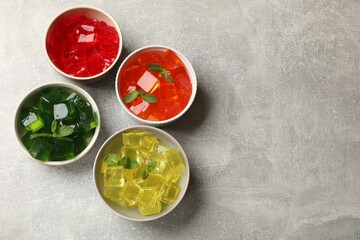 Different jelly cubes in bowls on grey table, flat lay. Space for text