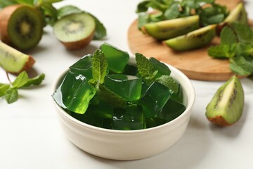 Obraz premium Delicious green jelly cubes in bowl, mint and kiwi on white table, closeup