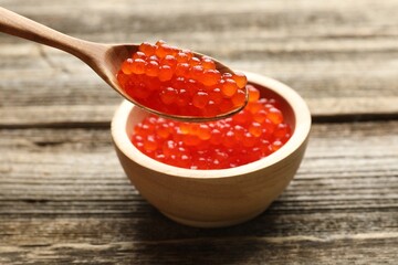 Taking red caviar with spoon from bowl at wooden table, closeup