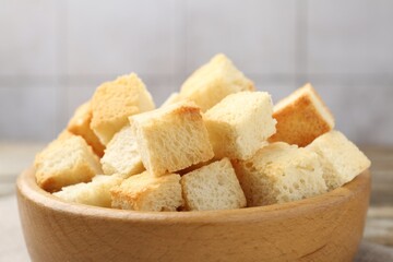 Tasty crispy croutons in bowl against blurred background, closeup