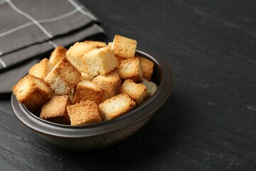 Tasty crispy croutons in bowl on dark textured table, closeup. Space for text