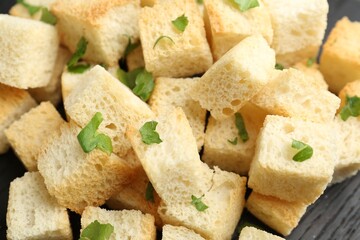 Tasty crispy croutons with cut parsley on black wooden table, closeup