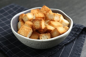 Tasty crispy croutons in bowl on dark textured table, closeup