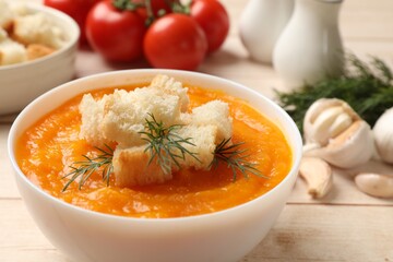 Delicious pumpkin cream soup with croutons, dill and ingredients on wooden table, closeup