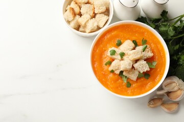 Delicious pumpkin cream soup with croutons, parsley and ingredients on white table, flat lay. Space for text