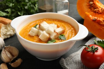 Tasty pumpkin cream soup with croutons and parsley in bowl among other products on dark table, closeup