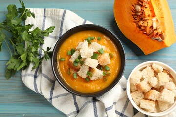 Tasty pumpkin cream soup with croutons, green onion and parsley on light blue wooden table, flat lay