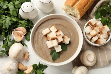 Delicious mushroom cream soup with croutons, parsley and ingredients on light table, flat lay